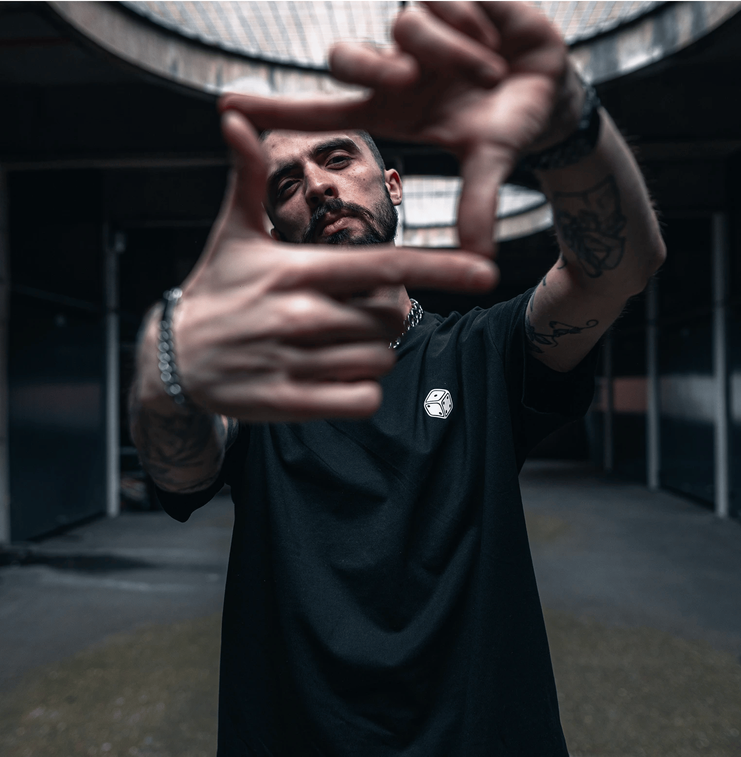A photograph of a man wearing an Adaki T-shirt creating a box gesture with his fingers, highlighting his face