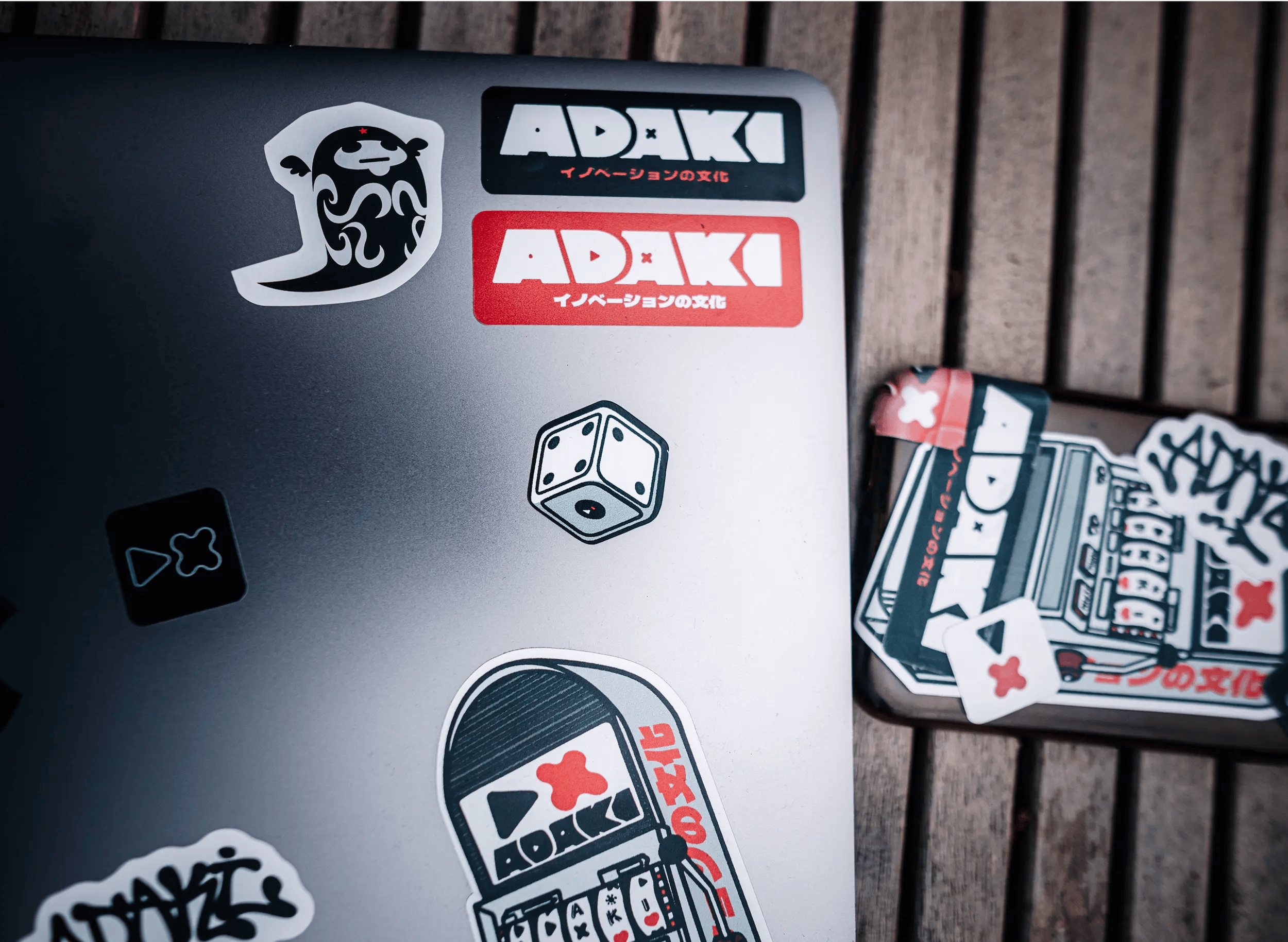 A top down photograph of a laptop and phone covered in Adaki Gambler Pack stickers